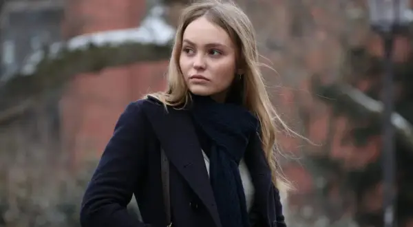 Lily-Rose Depp i en mörkblå kappa och halsduk, påminner om hennes roller i filmer.