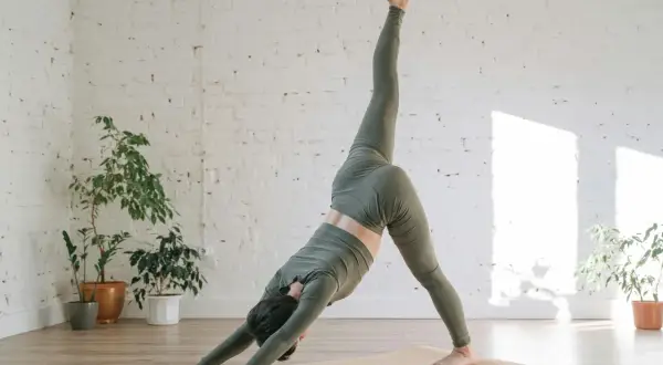 Mujer en postura de yoga de tres patas, explorando el vinyasa significado. El flujo dinámico se refleja en su movimiento.