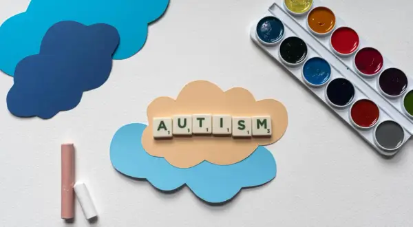 Litery układają słowo AUTISM na chmurce. Obok kredki i farby. Dzieci z autyzmem wysokofunkcjonującym mogą rozwijać się twórczo.