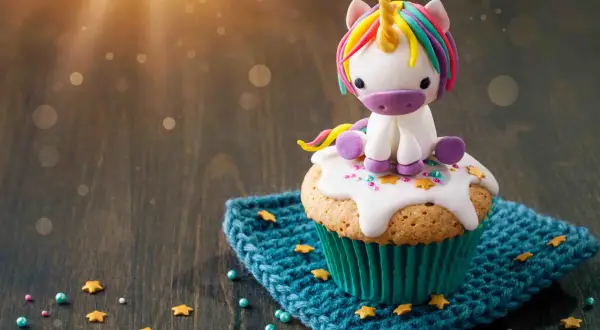 Un cupcake orné d'un adorable licorne en pâte à sucre, posé sur un glaçage blanc et des étoiles dorées. Le glaçage cupcake sucre glace est parfait pour une touche magique.