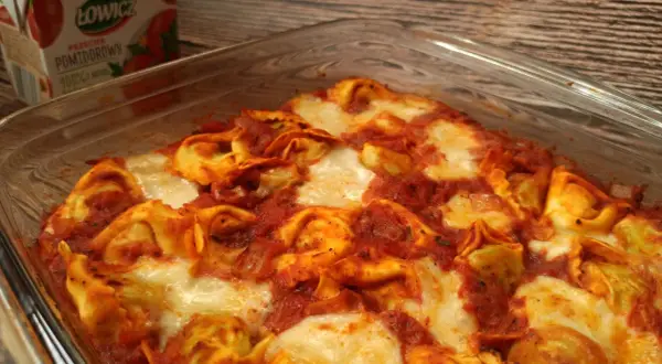 Pyszna zapiekanka z tortellini w sosie pomidorowym, zapieczona z serem. Obok kartonik przecieru pomidorowego Łowicz.