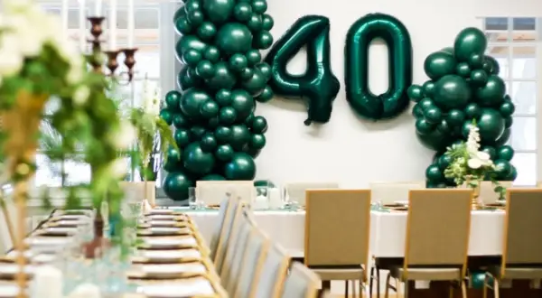 Uroczyste przyjęcie z okazji 40 urodzin. Zielone balony tworzą liczbę 40. Stół nakryty do eleganckiej kolacji.