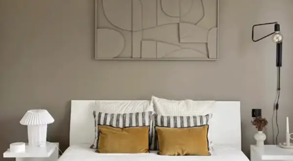 Une chambre moderne avec un lit blanc, des coussins moutarde et un tableau abstrait. Une belle idée tableau créatif pour une décoration murale apaisante.