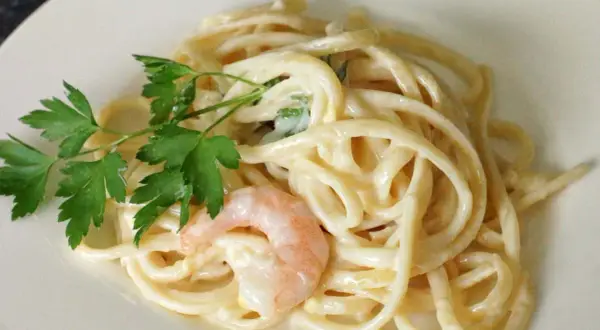 Cremige Pasta al Limone mit Garnelen und Petersilie auf einem weißen Teller. Ein Genuss für Augen und Gaumen.