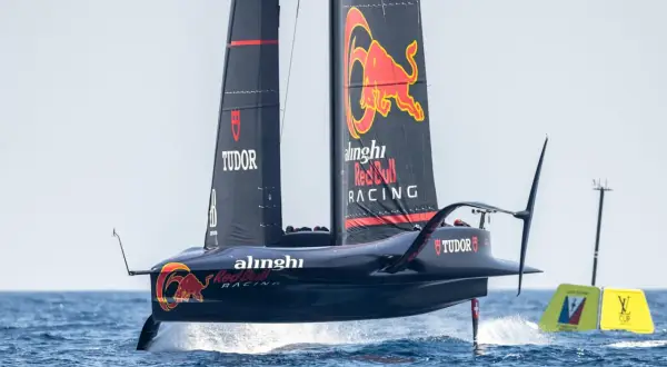 Wyścigowy jacht klasy AC75 z logo Red Bull Racing i Alinghi, unoszący się nad wodą na foilach.