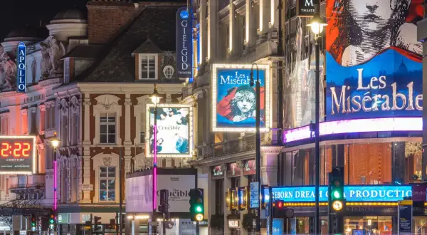 Nocne światła teatrów w londyńskim **West Endzie**: plakaty "Les Misérables", "The Crucible" i "2:22 A Ghost Story" oświetlają ulicę.