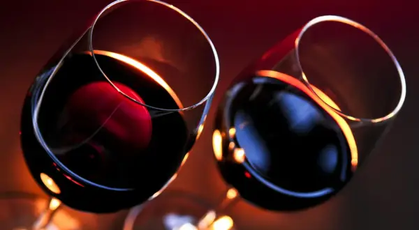 Dwa kieliszki z czerwonym winem, w blasku świec. Czy wino wytrawne jest zdrowe? Pytanie pozostaje otwarte.