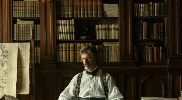 Mężczyzna w historycznym stroju siedzi w gabinecie pełnym książek, które mogą posłużyć jako inspiracja do seriali na podstawie książek.