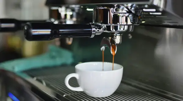 Macchina da caffè professionale eroga un espresso in tazza bianca. Il consumo di una macchina del caffè da bar varia, ma questa è un'immagine iconica.