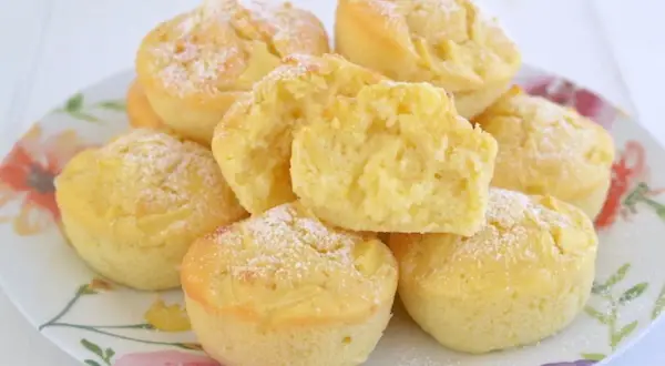 Muffin alle mele soffici e dorati, cosparsi di zucchero a velo, su un piatto fiorito. Uno è tagliato a metà, mostrando la morbida consistenza.