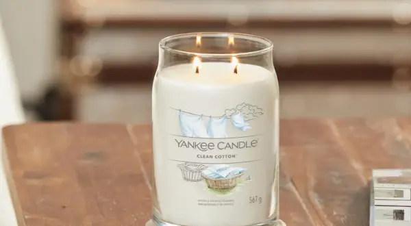 Zapalone świece zapachowe Yankee Candle Clean Cotton w szklanym słoju na drewnianym stole.