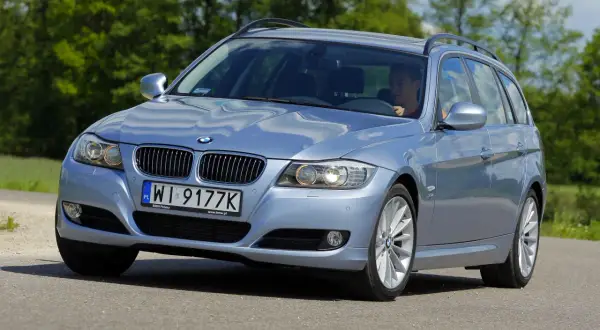 Błękitne BMW E91 na drodze, widać wyraźnie jego przednie światła i grill.