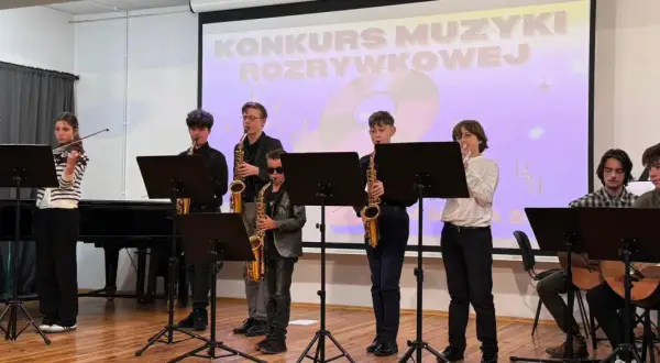 Młodzi muzycy grają na instrumentach: skrzypcach, saksofonach i gitarach, na tle ekranu z napisem "Konkurs Muzyki Rozrywkowej".