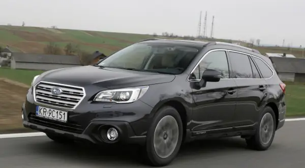 Ciemnoszary Subaru Outback 2025 na tle wiejskiego krajobrazu.