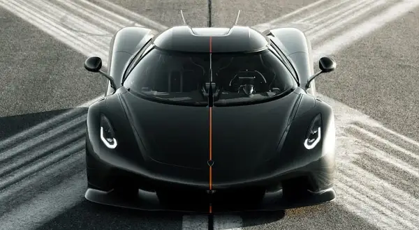 Czarny Koenigsegg Jesko z pomarańczowym pasem na masce, gotowy do startu na torze.