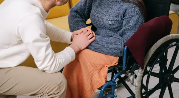 Uomo tiene la mano di una donna su sedia a rotelle, un gesto di supporto mentre si discute del pagamento invalidità civile.