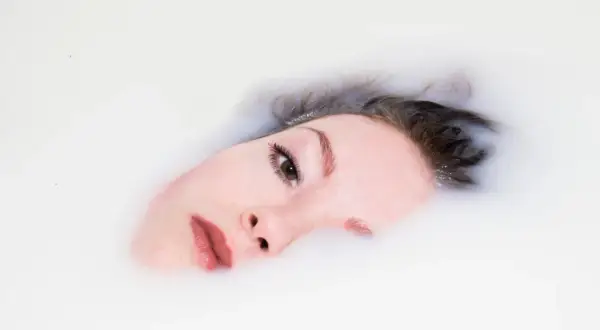 Delikatna twarz zanurzona w mleku, z włosami unoszącymi się na powierzchni. Ta high key fotografia podkreśla czystość i spokój.