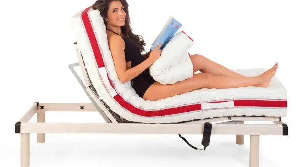 Donna sorridente legge un libro a letto, con il materasso regolabile che offre la postura corretta per guardare la TV o rilassarsi.