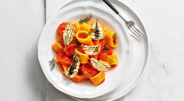 Piatto di pasta con pomodorini e croccanti alici fresche, guarnito con aneto.