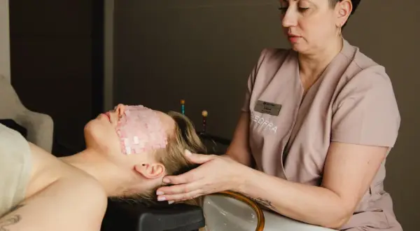 Relaks w gabinecie head spa. Kobieta leży z kamieniami na oczach, a masażystka delikatnie dotyka jej skroni.