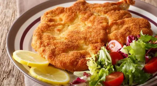 Chrupiący kotlet milanese z cytryną i świeżą sałatką z pomidorkami.