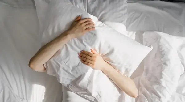 A person clutches a pillow in bed, sunlight dappling the sheets. This scene evokes the struggle many with ADHD face: do people with ADHD have trouble sleeping?