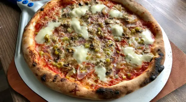 Chrupiąca pizza z pieca kamiennego z serem, pieczarkami i oliwkami na łopacie.