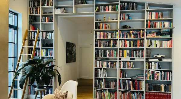 En stor inbyggd bokhylla med en stege, fylld med böcker och prydnadssaker. Perfekt inbyggd bokhylla inspiration för ett bibliotek.