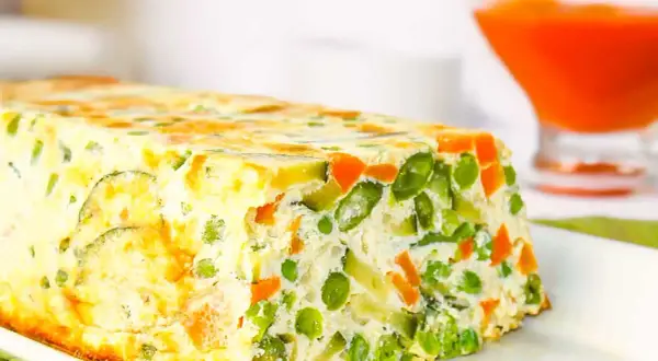 Un delicioso pastel de verduras, con guisantes, zanahoria y calabacín, horneado en un molde rectangular.