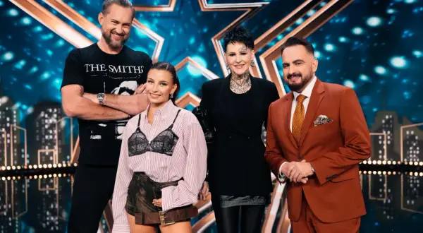 Cztery osoby stoją na scenie z gwiazdą w tle. To jury Mam Talent.