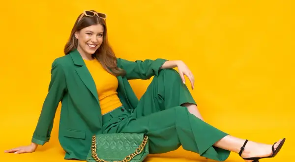 Eleganckie czarne sandałki na obcasie idealnie pasują do zielonego garnituru damskiego. Modelka prezentuje stylizację z żółtym topem i zieloną torebką.