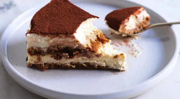 Una fetta di tiramisù, con cacao in polvere, su un piatto. La ricetta perfetta per un dolce cremoso e goloso.