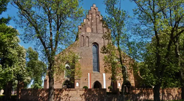 Gotycka ceglana świątynia, prawdopodobnie kościół pw. św. Jadwigi, otoczona zielenią. W tle błękitne niebo. Halszka Szamotuły.
