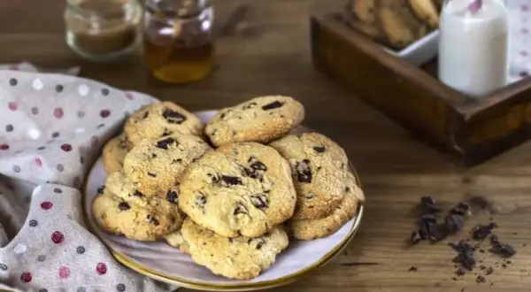 Montón de galletas con pepitas de chocolate recién horneadas, listas para disfrutar con un vaso de leche.