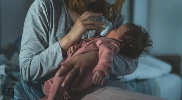 Zmęczona mama karmi butelką niemowlę, które obudziło się w nocy i nie śpi 2 godziny.