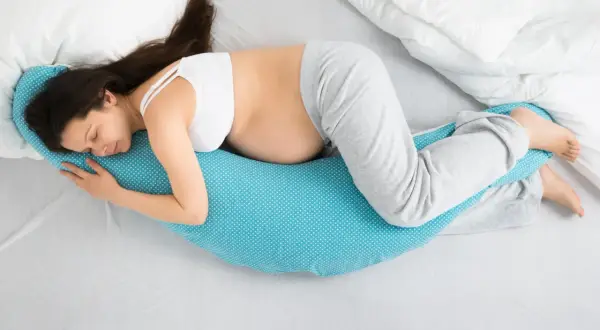 Mujer embarazada duerme de lado, abrazando una almohada de apoyo. Las posturas de dormir en el embarazo son clave para el descanso.