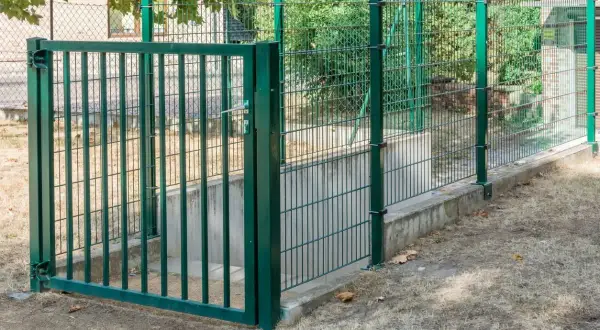 Grüner doppelstabmattenzaun mit Tor, der eine Treppe zu einem Kellerabgang sichert. Die Montage ist solide und schützt den Eingang.