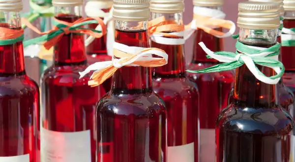 Rzędy butelek z rubinowym winem z rabarbaru, ozdobione kolorowymi wstążkami.
