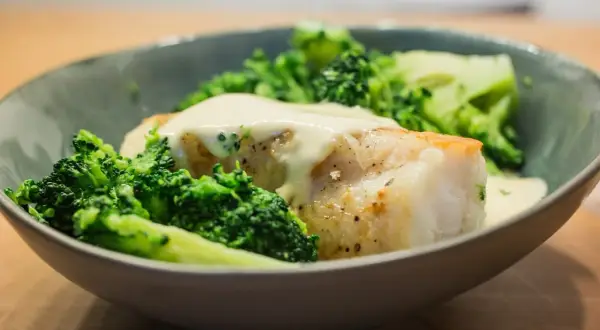 Un plat de queue de lotte poêlée, nappée d'une sauce crémeuse et accompagnée de brocolis croquants.