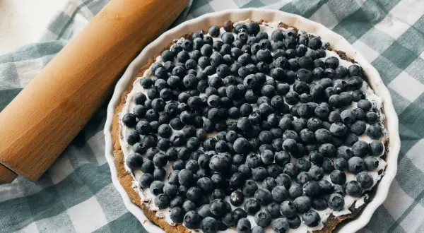 Pyszna tarta z borówkami i kremowym mascarpone, gotowa do pieczenia. Obok wałek do ciasta.