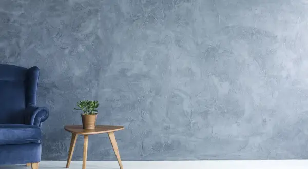 Fauteuil bleu profond devant un mur texturé en **stucco mur**. Une petite plante verte repose sur une table d'appoint en bois.