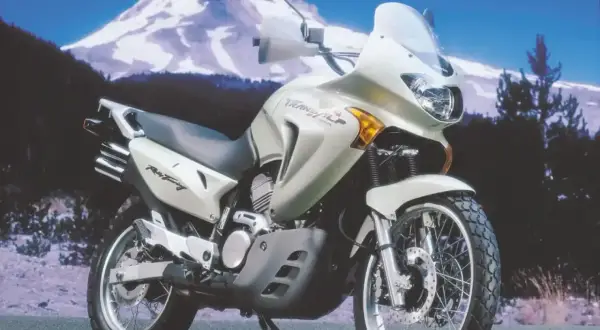 Jasnosrebrny motocykl Honda Transalp 650 gotowy na przygodę na tle ośnieżonej góry.