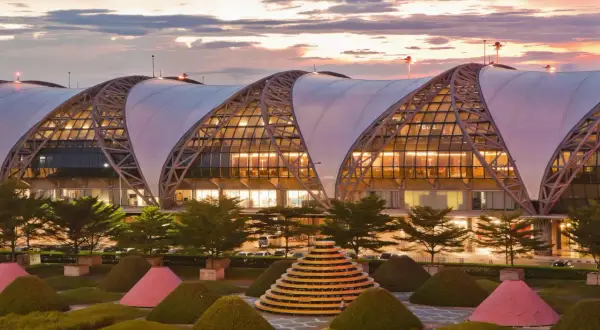 Der moderne Flughafen Bangkok Suvarnabhumi mit seiner markanten Dachkonstruktion und der kunstvollen Gartenanlage bei Sonnenuntergang.