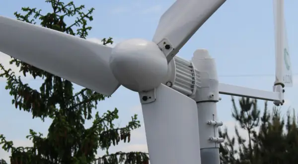Montaż elektrowni wiatrowej w pobliżu drzew. Białe łopaty wirnika i gondola na tle błękitnego nieba.