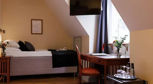A hotel room with a bed, desk, chair, and a TV mounted on the wall.