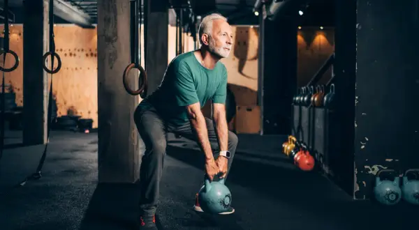Älterer Mann trainiert mit Kettlebell, stärkt seine bauchmuskeln im Fitnessstudio.