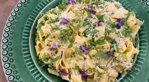 Krämig sparris pasta med färska örter och violblommor, toppad med riven parmesan. En härlig vårrätt!