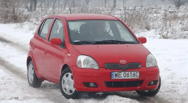 Czerwona Toyota Yaris 1 na śniegu. Kierowca przygotowuje się do wymiany żarówki.