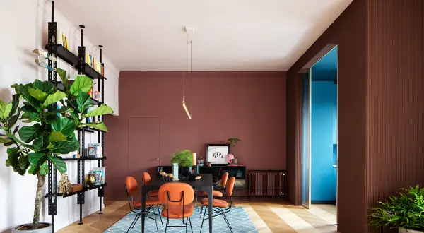 Un soggiorno moderno con pareti color mattone, sedie arancioni vivaci e un tappeto blu. Un esempio di come abbinare il color mattone con tocchi audaci.