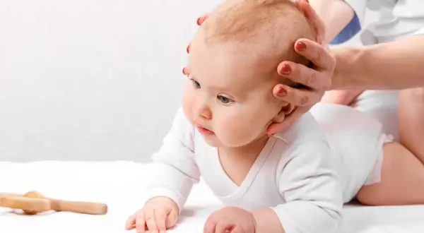 Dziecko na brzuchu, ręce terapeuty delikatnie dotykają główki. Zwrócono uwagę na szybko zarastające ciemiączko, skutki obserwacji.